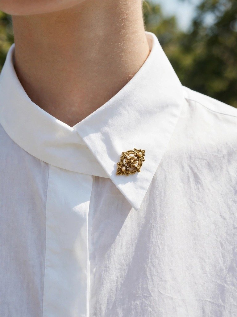 Small vintage gold brooch pinning one collar point of a crisp white shirt closed